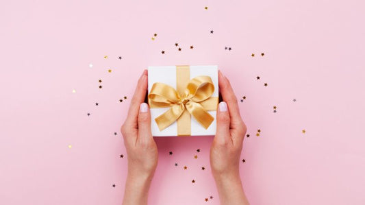 Hands holding a white gift box with a gold bow.